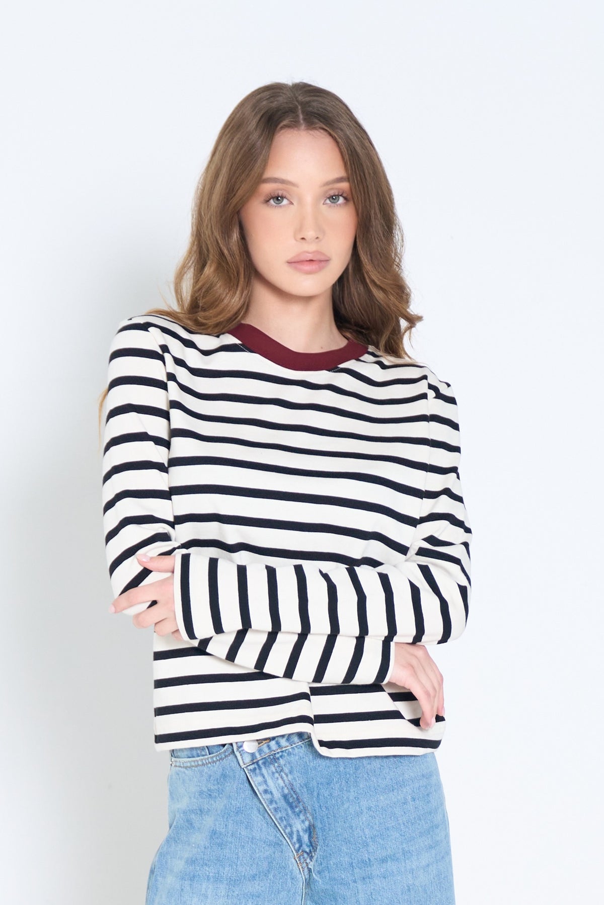 Woman wearing a black and white striped sweater with a maroon collar against a white background